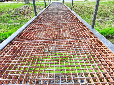 Beautiful perspective photo of rusty Iron pedestrian bridge with grass background. CLOSE-UP. Photo is taken on a cloudy day in spring. High quality photo