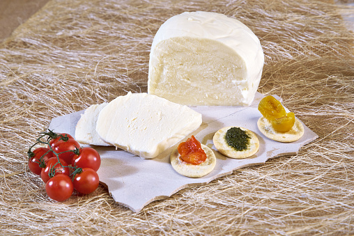 Sliced ​​fresh cheese on a white stone plate with cherry tomatoes and bruschetta