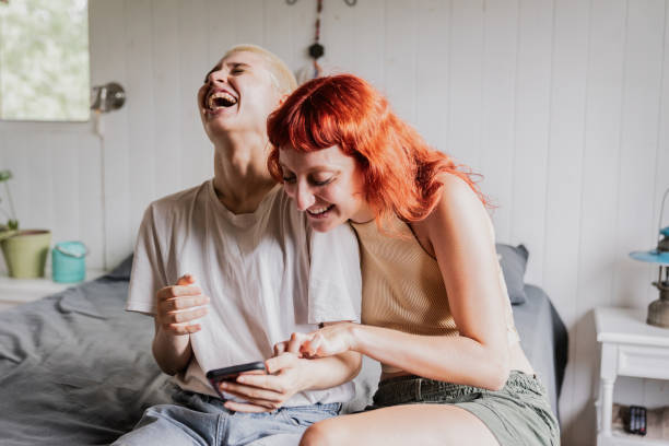 female friends using mobile phone on bedroom at home - tiener fotos stockfoto's en -beelden