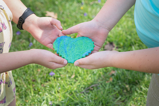 Children's hands holding a heart shaped, green and blue sugar cookie at Earth Day celebration.