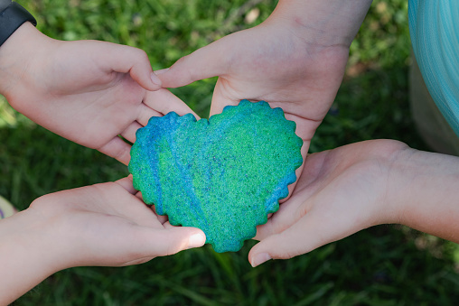 Children's hands holding a heart shaped, green and blue sugar cookie at Earth Day celebration.
