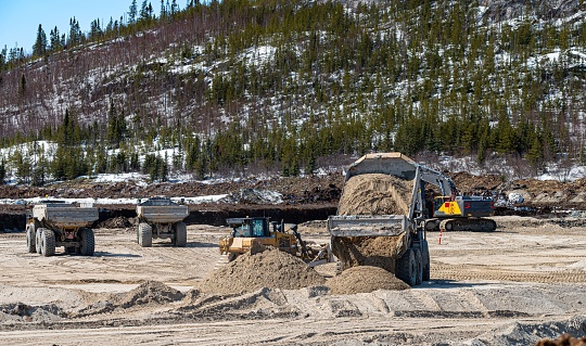 Three dump trucks with a bulldozer and an excavator on a construction site, during spring