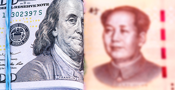 Folded american dollars banknotes with Benjamin Franklin portrait wrapped by rubber band and chinese banknote with Mao Zedong portrait. Selective focus