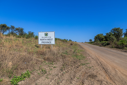 Wide shot of a sign reading Welcome to North West Province with a gravel road to the right of it.  Copy space to the right.