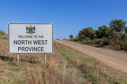 Landscape of a gravel road with a road sign reading Welcome to the North West Province. Copy space to the right.