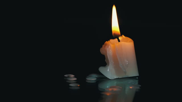 One Short Paraffin Candle Burns on Black Background with Reflection