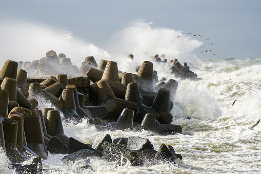 Storm at sea, high waves crashing against the concrete breakwaters of the port, high white splashes