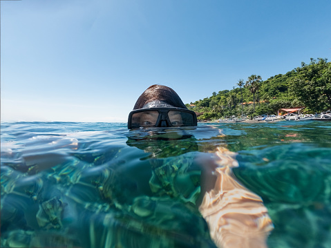 A solo senior Chinese woman takes a selfie while snorkeling off a local beach in Amed, Bali, Indonesia.