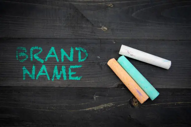 Photo of Brand Name. Text and pieces of chalk on a dark wood texture background