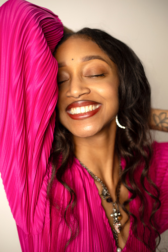 African-American woman with wavy hair and pink blouse smiling with eyes closed and one arm lifted upward