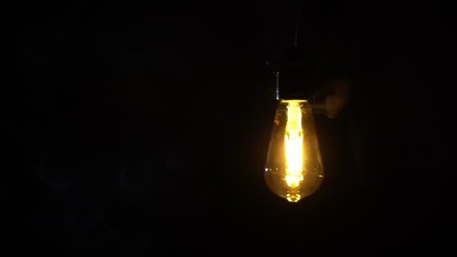 Antique Light Bulb Flashes Orange in Fog on Black Background