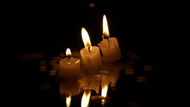 Three Paraffin Candles Burn in a Row on a Black Background with Reflection