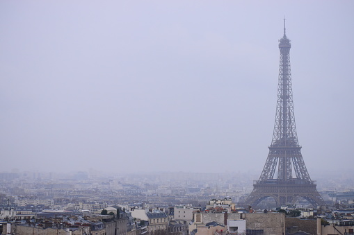 Horizontal shot of the Eiffel Tower as it towers over other buildings on a foggy day.