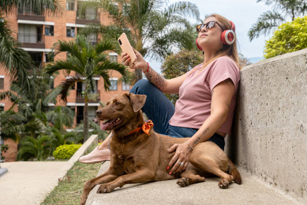 mujer de mediana edad disfrutando al aire libre y escuchando música, acompañada de su mascota en la ciudad tropical. - pampered pets audio fotografías e imágenes de stock
