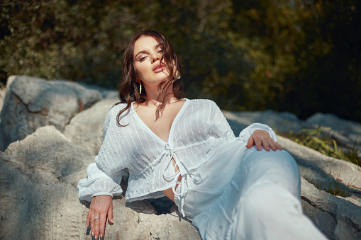 A woman in a white dress lying on a rock in the forest.