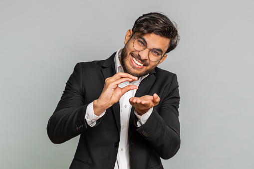 Need some more, please give me. Indian businessman showing a little bit gesture with sceptic smile showing minimum sign, measuring small size, begging help. Arabian man guy on gray studio background