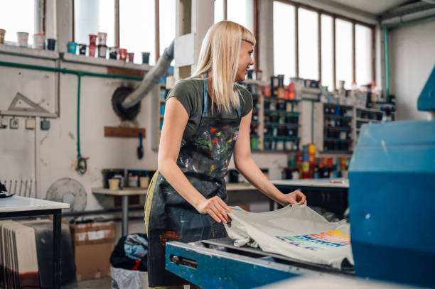 istock Female printer putting silkscreen printed t-shirt into drying machine. 2133994760