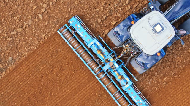 AERIAL Drone Top Down Shot of Blue Tractor Preparing Field for Sowing in Village