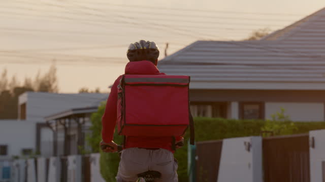 A man in a red jacket is riding a bicycle with a red box on his back