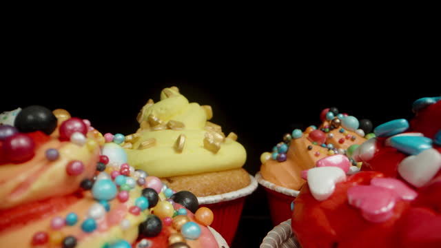 Festive homemade cupcakes, each individually decorated with various sprinkles in the form of balls and hearts. Dolly slider, close up.