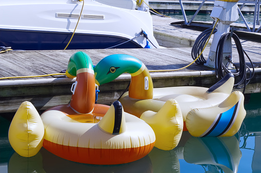 Waterfront with a wooden dock, docked yacht boat and yellow inflatable duck-shaped swimming floats.