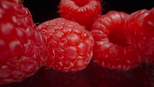 Raspberries scattered on a black mirrored table, slow dolly. Macro shot.