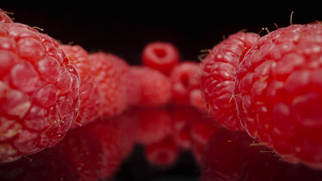 Red raspberries arranged on a black mirrored table. Dolly slider, close up.