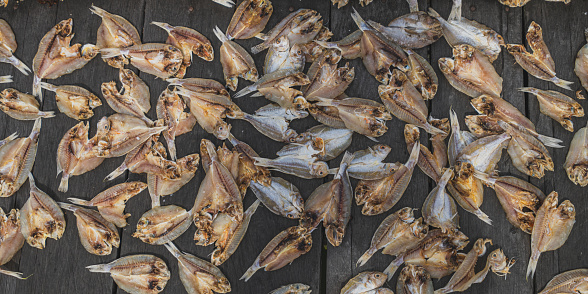 Several whole dried fish are scattered across a rustic wooden table. Their brown, scaly bodies are wrinkled and their fins are curled.