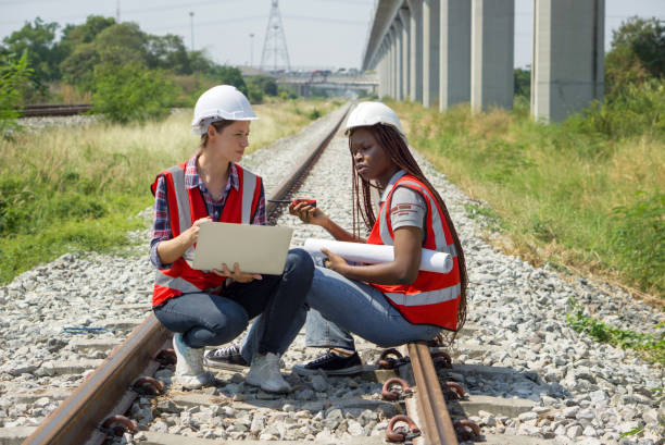 istock Two engineer with safety helmet and high-visibility vest reviewing work to be done on a railway track project while holding a set of plans or blueprint, walkie-talkie and laptop computer. 2134320816