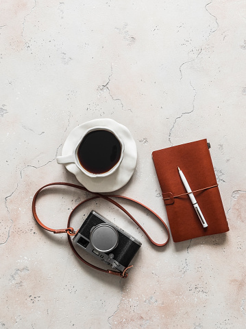 A retro style camera, a cup of coffee, a leather-bound diary on a light background, top view