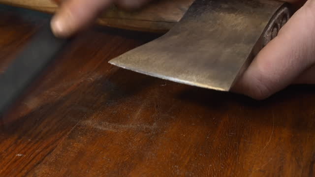 Tool closeup: Man sharpens old axe edge with whetstone on countertop