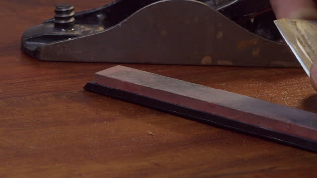 Man sharpens wood plane blade on countertop whetstone, close-up view