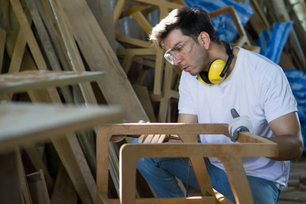 A man is focused as he shapes a piece of wood with his tools in a workshop setting. Side view