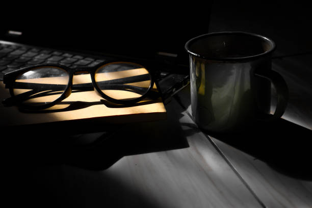 Cup of tea or coffee, e-reader and reading glasses on the table. Pile of books in the background. Selective focus.