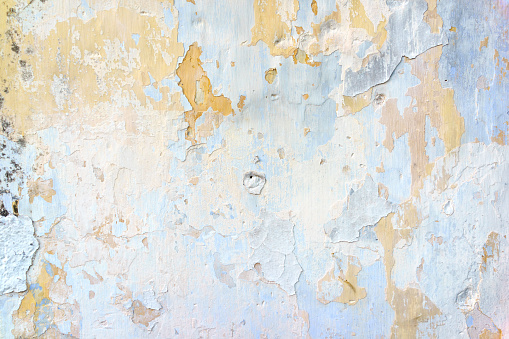 Closeup of badly fixed building facade wall covered with cracks in stucco and paint.