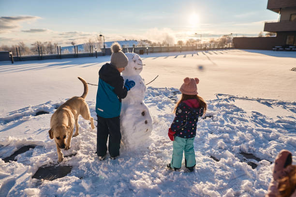 Winter portrait of a beautiful boy and girl’s laughing and having a lot of fun in snow. They are making a snowman.