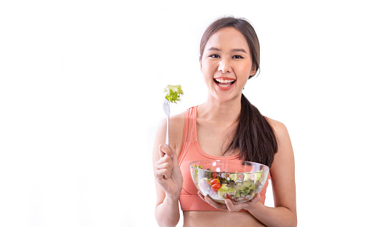 Asian woman in sportswear holding bowl of fresh salad for healthy eating and vegan culture of consumption usage