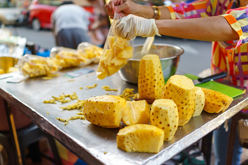 A street vendor stall sells freshly cut pineapple packed in plastic bags.
