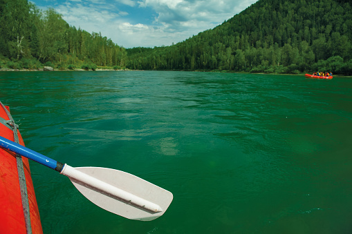 Paddle and side of the boat. River with green water. The concept of boating and rafting.