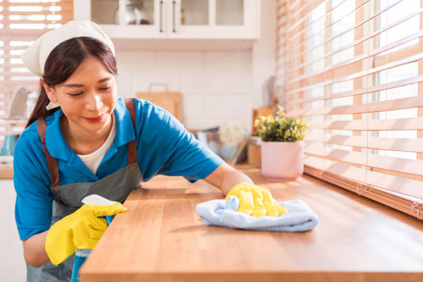 professional asian woman cleaning service wearing yellow rubber gloves, using a rag to wipe with spraying liquid detergent on the wooden top kitchen counter at home. housekeeping cleanup, cleaner. - cleaning domestic kitchen counter top housework stock-fotos und bilder