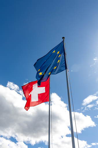 Flags of Switzerland and EU blowing in the wind under sunny blue sky