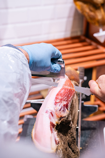 Hand cutting prosciutto with a knife.