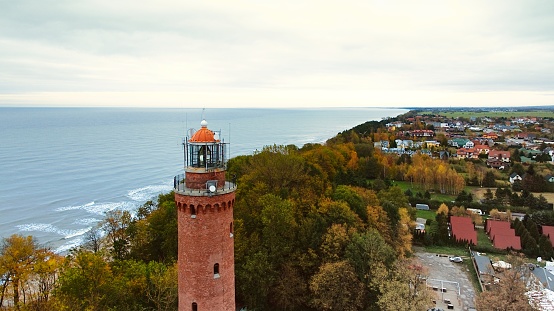 Drone-captured image of Gski Lighthouse, Poland, on a cloudy November day. The serene sea, gentle waves, and empty beach create a tranquil coastal scene, offering a peaceful retreat by the Baltic.