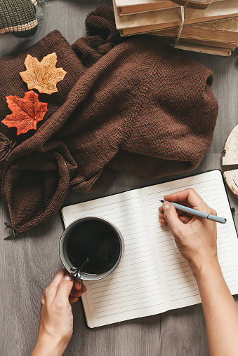 woman hands knitting dark brown sweater and taking notes