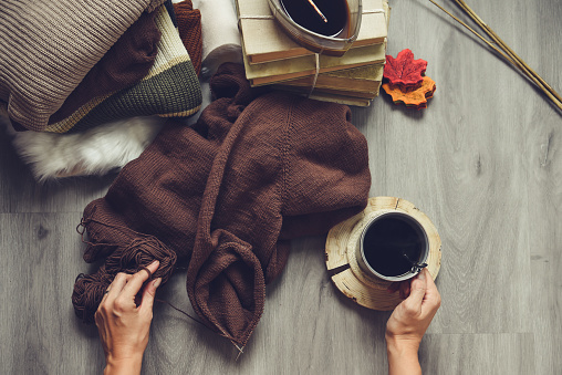 woman hands knitting dark brown sweater and taking notes