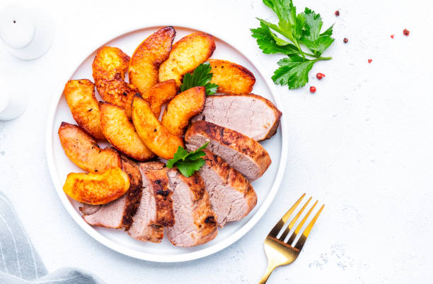 Baked pork tenderloin with caramelized apples on plate, white table background, top view