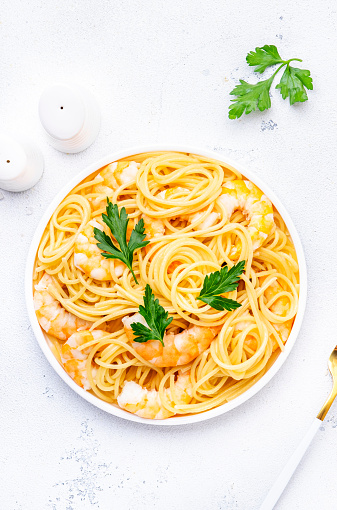 Spaghetti pasta with big shrimp, olive oil and parsley on white table background. Top view