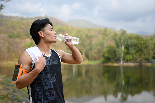 Shot of male runner resting and drinking water from a bottle for hydration after exercising.
