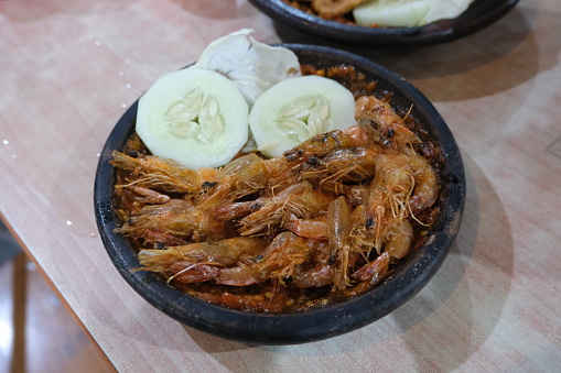Sizzling shrimp platter with fresh cucumber and spicy sambal, served in a hot stone bowl.