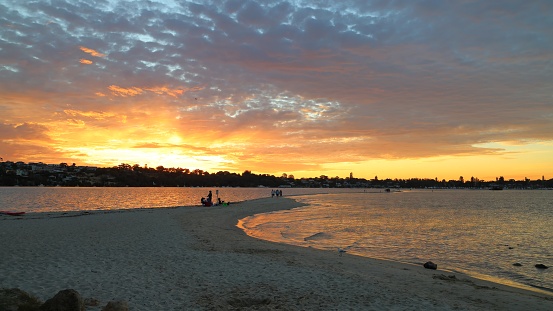 Tourists walking on the long sandbank (sandbar) stretching into the Swan River at Point Walter, Perth, Western Australia. Sunset, golden hour.